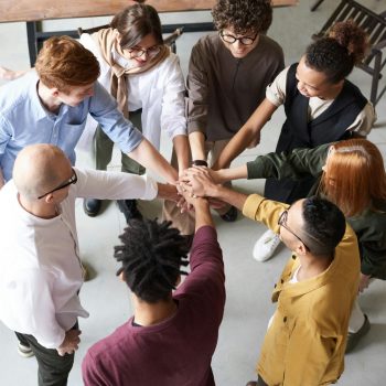 A diverse group of professionals joins hands in a team-building exercise indoors.
